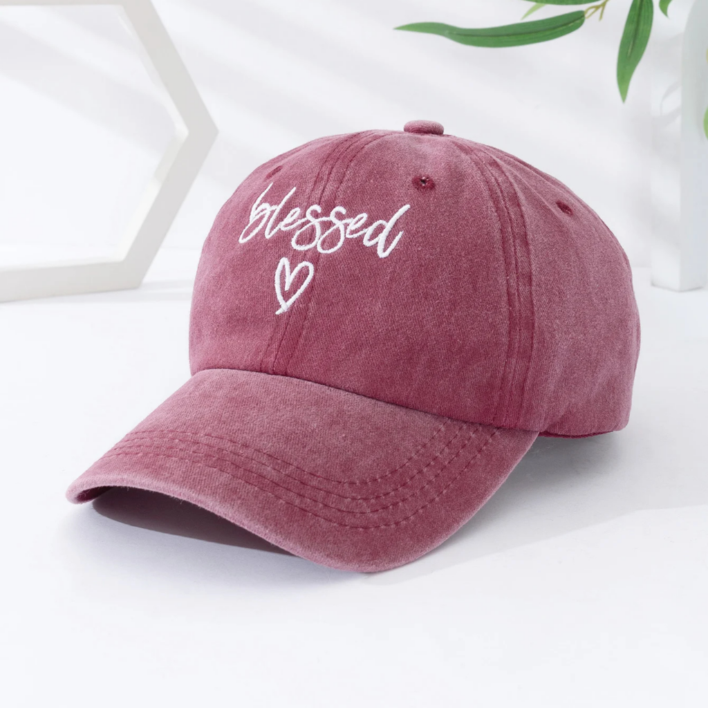 Casquette en Jean Délavée avec une Inscription et un Cœur posée sur une table blanche avec des feuilles et un motif en fond