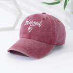 Casquette en Jean Délavée avec une Inscription et un Cœur posée sur une table blanche avec des feuilles et un motif en fond
