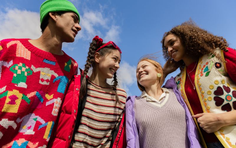 Groupe de 4 jeunes habillé chacun d'un style différent, très coloré, ils se regardent avec un grand sourire chacun.